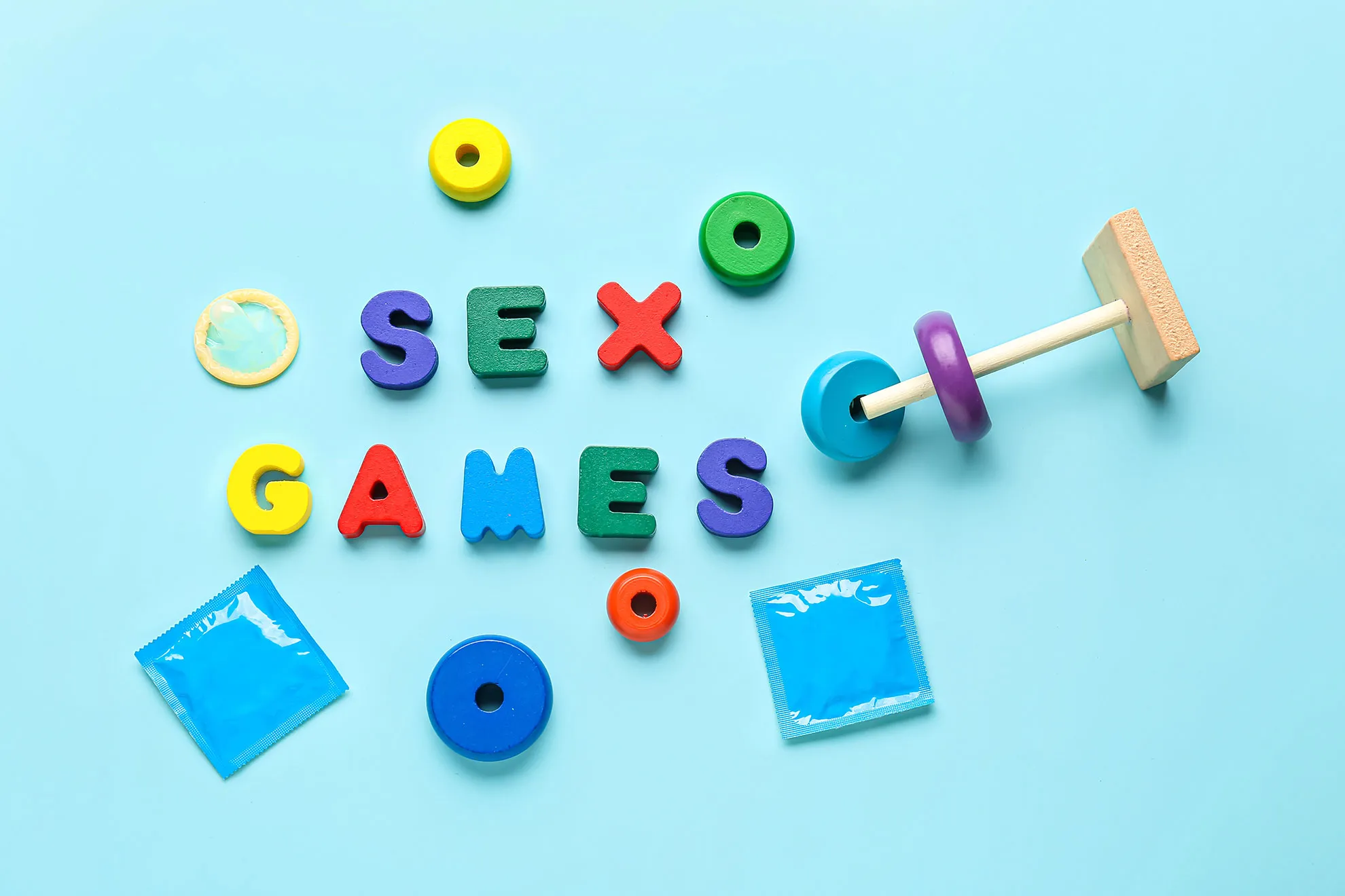 Värikkäät SEX GAMES -leikkikirjaimet, kondomeja ja puinen palikkapeli vaaleansinisellä taustalla — humoristinen lähestymistapa aikuisten peleihin